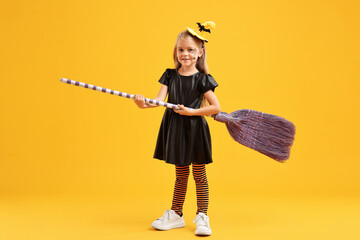 Wall Mural - Funny girl with broom dressed like witch on yellow background. Halloween celebration