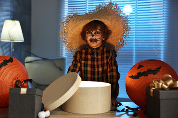 Wall Mural - Cute boy dressed like scarecrow with festive decor and gift boxes indoors at night. Halloween celebration