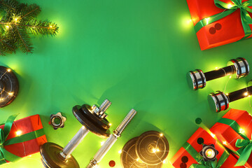 Poster - Dumbbells, fir tree branches, gift boxes and Christmas lights on green background, flat lay. Space for text