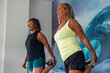 © EDER - Two elderly women smiling in sportswear stretching quadriceps during gym training routine