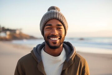 Wall Mural - Portrait of a content afro-american man in his 20s donning a warm wool beanie in front of sandy beach background