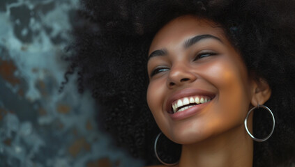 A joyful woman with a stylish afro laughs in front of a blue wall