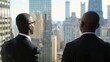 © vefimov - Two African American businessmen standing side by side, wearing suits, looking out over city skyline.