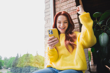 Sticker - Portrait of nice young girl sit window use phone raise fist wear yellow sweater loft interior flat indoors