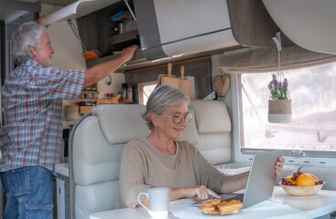 Sticker - Relaxed senior couple in travel vacation leisure inside a camper van dinette enjoying breakfast together while wife uses laptop