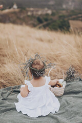 Little girl in white dress sitting on the hill with basket with meal at sunset. Happy childhood. picnic in the field.