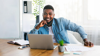 Poster - Portrait of young successful businessman sitting at his worplace in modern office and posing to camera, copy space