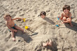 © Oriol Roca - Little brothers pose contentedly after burying their older brother in the sand on the beach with their shovels.
