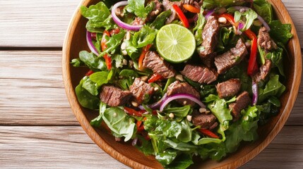 Wall Mural - Close-up of a Thai beef salad with mixed greens, red onions, and a zesty lime dressing, arranged on a light wooden table.