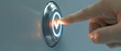 © Arnon  Parnnao - Finger pressing a modern push button with glowing light on a gray background.