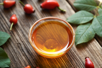 Wall Mural - A bowl of rosehip seed oil with fresh rose hips on a table