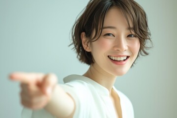a cheerful japanese woman in her early 20s smiles and points at the viewer with one hand, dressed in