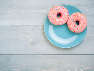 Wall Mural - Top view of two pink donuts on gray wooden background with copy space. Colorful donuts on plate with copyspace. Glazed doughnuts with sprinkles on grey wooden table. Smile sign, good morning concept