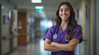 © Creative Art7 - A beautiful young nurse in purple scrubs stands with her arms crossed and smiles at the camera, standing in a hospital background