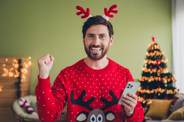 Sticker - Photo of nice young man hold smart phone raise fist ugly sweater christmas time apartment indoors