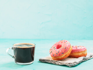 Two pink donuts and coffee on blue concrete background with copy space. Colorful donuts and coffee cup with copyspace. Glazed doughnuts with sprinkles