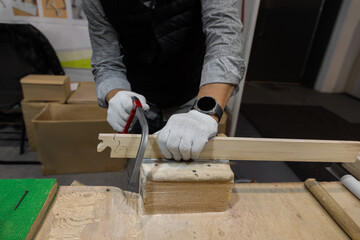 male hands in work gloves sawing wooden blank with thin hand saw