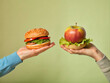 © MihaForPeace - an apple in one hand and a hamburger in the other. This shows the contrast between healthy, fresh vegetarian food and unhealthy, processed fast food. It highlights choices in nutrition, diet, and fitn