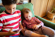 © Marko Geber - Little brother and sister using smartphones together on sofa