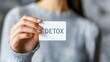 © TENTIP - Close-up of a person holding a card with the word 'DETOX' written on it, promoting health, wellness, and a clean lifestyle.