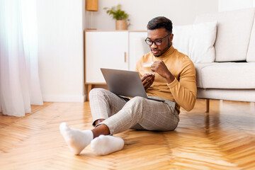 Aufkleber - Afro Man Working On Laptop Having Coffee Sitting On Floor At Home. Freelance Career And Lifestyle. Selective Focus