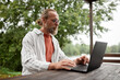 © Seventyfour - Side view portrait of bearded adult man using computer while working outdoors at terrace by beautiful lake in nature copy space