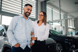 © Zamrznuti tonovi - Happy couple sharing moment in bright dealership with new car