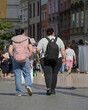 © Oleksandr Bochkala - City bustle: Two women, one of whom is overweight, walk along a picturesque street with backpacks, European architecture, the dynamic pace of everyday life