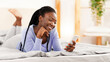 © Prostock-studio - Positive Black Girl Using Smartphone Lying In Bed At Home In The Morning. Selective Focus