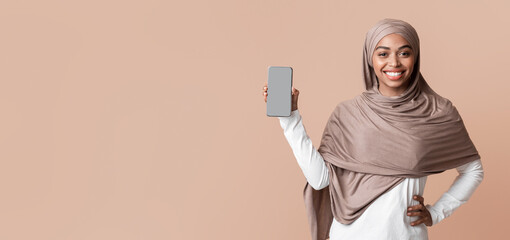 Poster - Happy afro muslim woman in hijab demonstrating modern smartphone with blank screen for mockup, posing over yellow background, free space