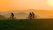 © helivideo - AERIAL, SILHOUETTE, LENS FLARE: Cyclists riding along a scenic hilltop at sunset. Vibrant glowing orange sky and the sheer beauty of an evening outdoor adventure in a picturesque country setting.