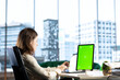© DC Studio - Young business entrepreneur looking at green screen mockup on her gadgets, working in modern urban corporate office. Female leader developing a strategy to increase funding for success.