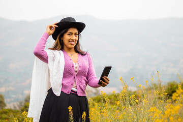 Foto de una feliz y bonita campesina con un sombrero hablando por un teléfono celular en los Andes peruanos. Mujer usando teléfono móvil