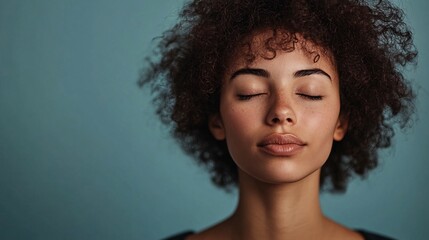 Wall Mural - Young woman with curly hair posing with closed eyes against a blue backdrop