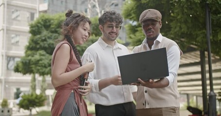 Poster - In a contemporary urban environment, three colleagues work together on a laptop outdoors, demonstrating effective teamwork and the integration of technology within a professional setting.