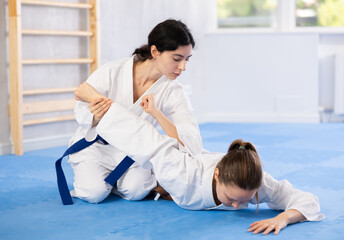 Wall Mural - Woman holds her opponent by force while sitting on mats during judo classes