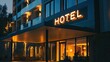 © Pricha.RT - An elegant hotel exterior with an illuminated 'HOTEL' sign at night. The buildings facade is lit, showcasing its modern design and welcoming atmosphere.