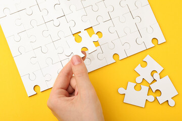 Wall Mural - Woman solving white puzzle on yellow background, closeup