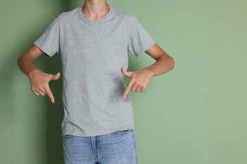 Canvas Print - Teenage boy wearing light grey t-shirt on green background, closeup. Space for text