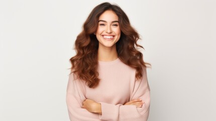 Canvas Print - A young woman with long, wavy hair and a soft, appreciative smile, wearing a light pink sweater, stands confidently with her arms crossed against a light background.