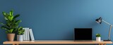 Modern workspace with a blue wall, wooden desk, laptop, books, and a stylish lamp, perfect for productivity and inspiration.