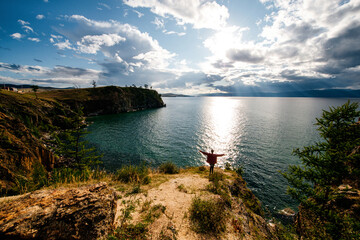 a girl at sunset stands at a cliff and admires the sunset on Lake Baikal