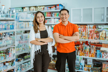 two smiling business owners stand with crossed hands inside a supermarket