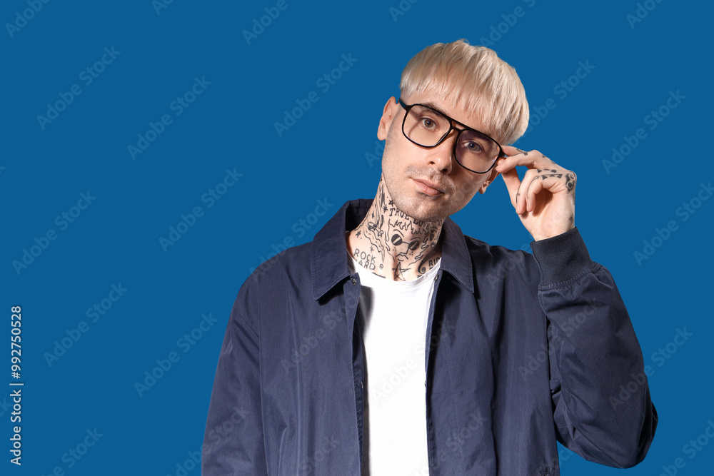 Young tattooed man in eyeglasses on blue background