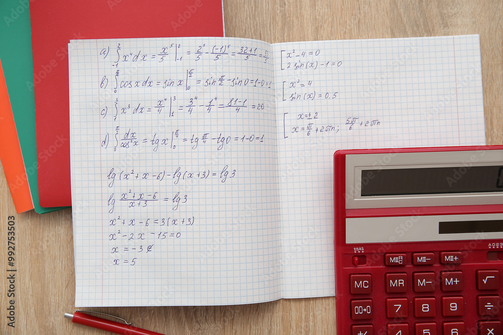 Open copybook with math formulas and calculator on wooden table