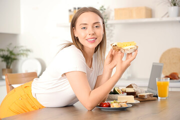 Wall Mural - Beautiful young happy woman holding tasty toast with fresh butter and cheese in kitchen at home