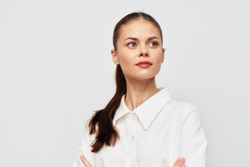 Wall Mural - confident young woman with long brown hair wearing a white shirt, looking thoughtfully to the side against a plain light background Portrait emphasizing poise and contemplation