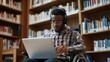 © Yulia - Portrait of young African-American man in wheelchair in headphones with laptop at college library