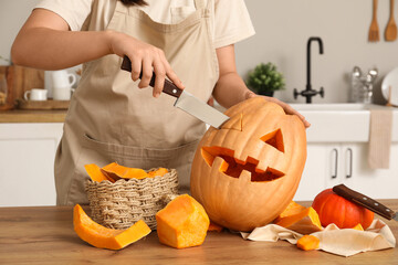 Woman carving Jack-O-Lantern pumpkin with knife for Halloween on counter in kitchen