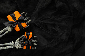 Wall Mural - Halloween gifts, skeleton hands and tulle on black background. Top view